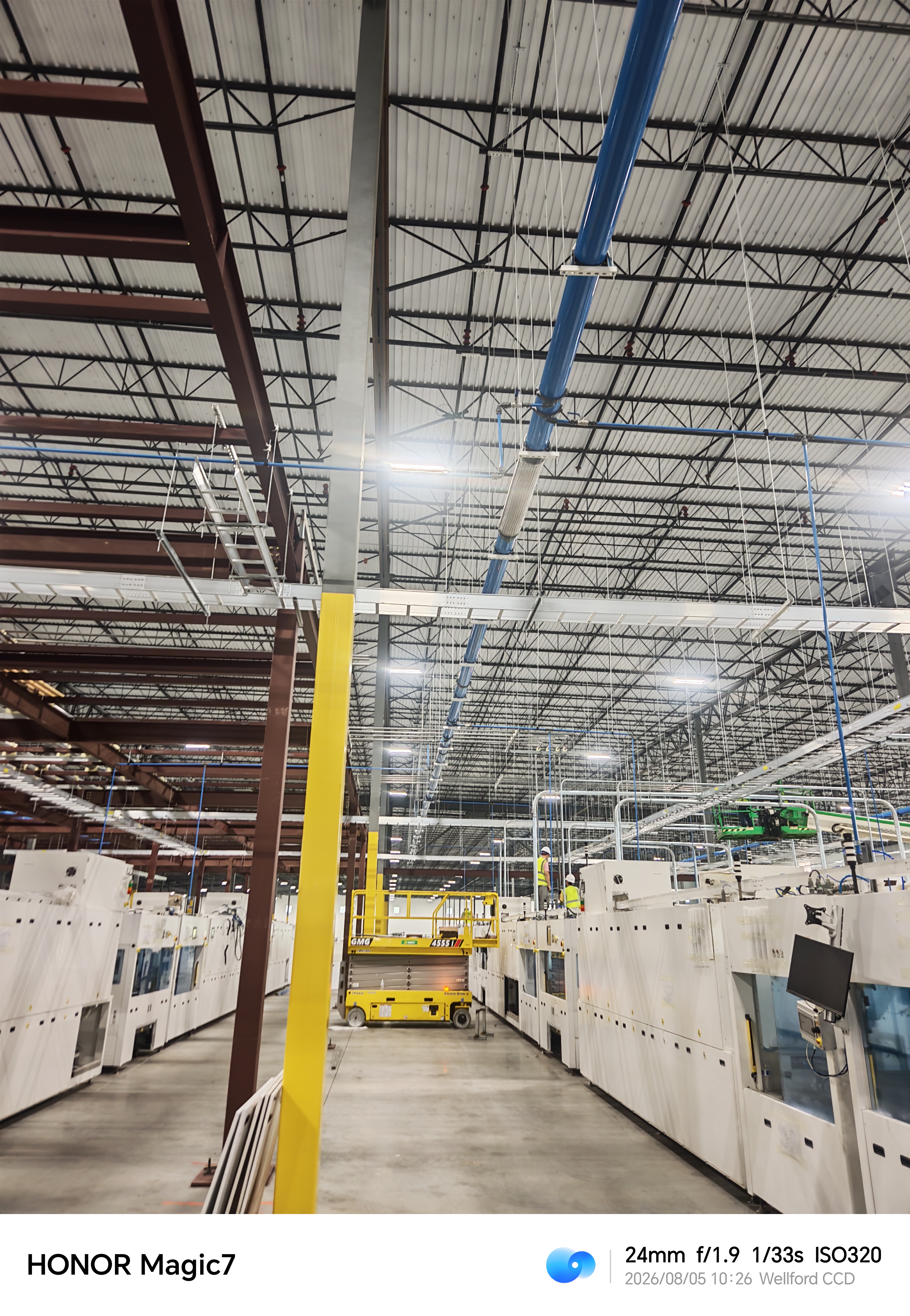 Industrial facility interior with overhead pipework and installation crews